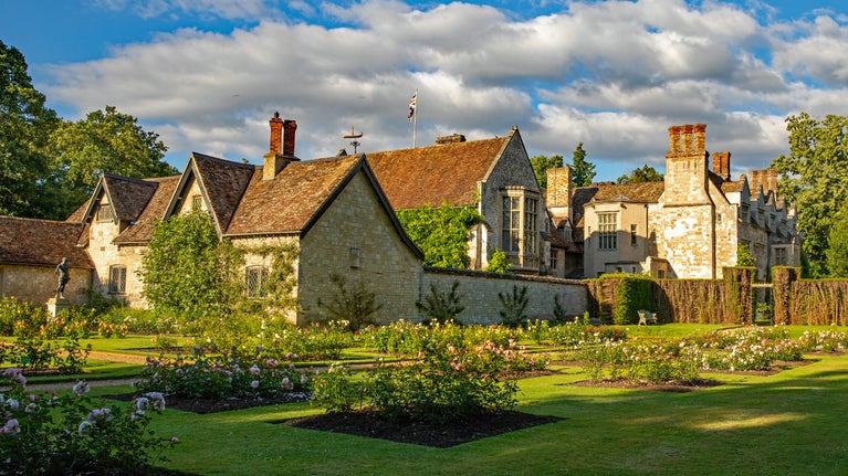 The extended Rose Garden at golden hour at Anglesey Abbey. A view onto the house with the roses lit up in the sunlight.